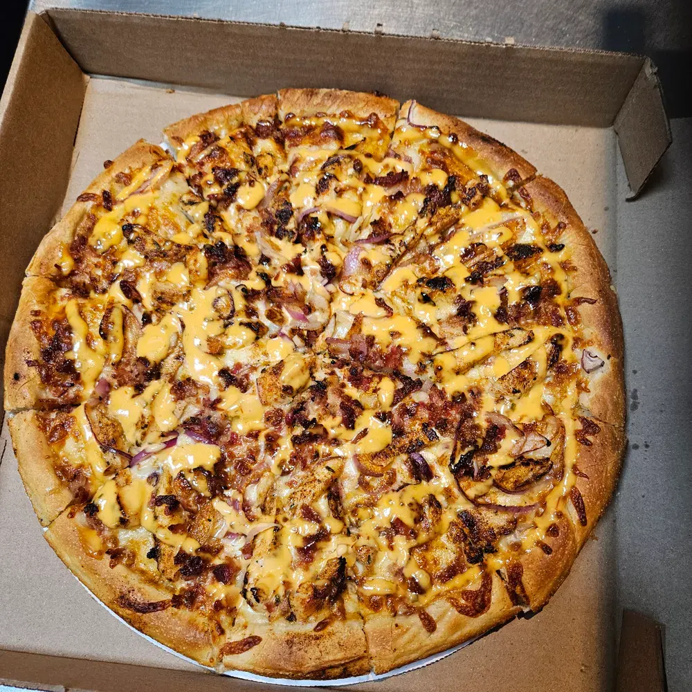 Pizza topped with grilled chicken, bacon, red onion and a cheese-sauce drizzle